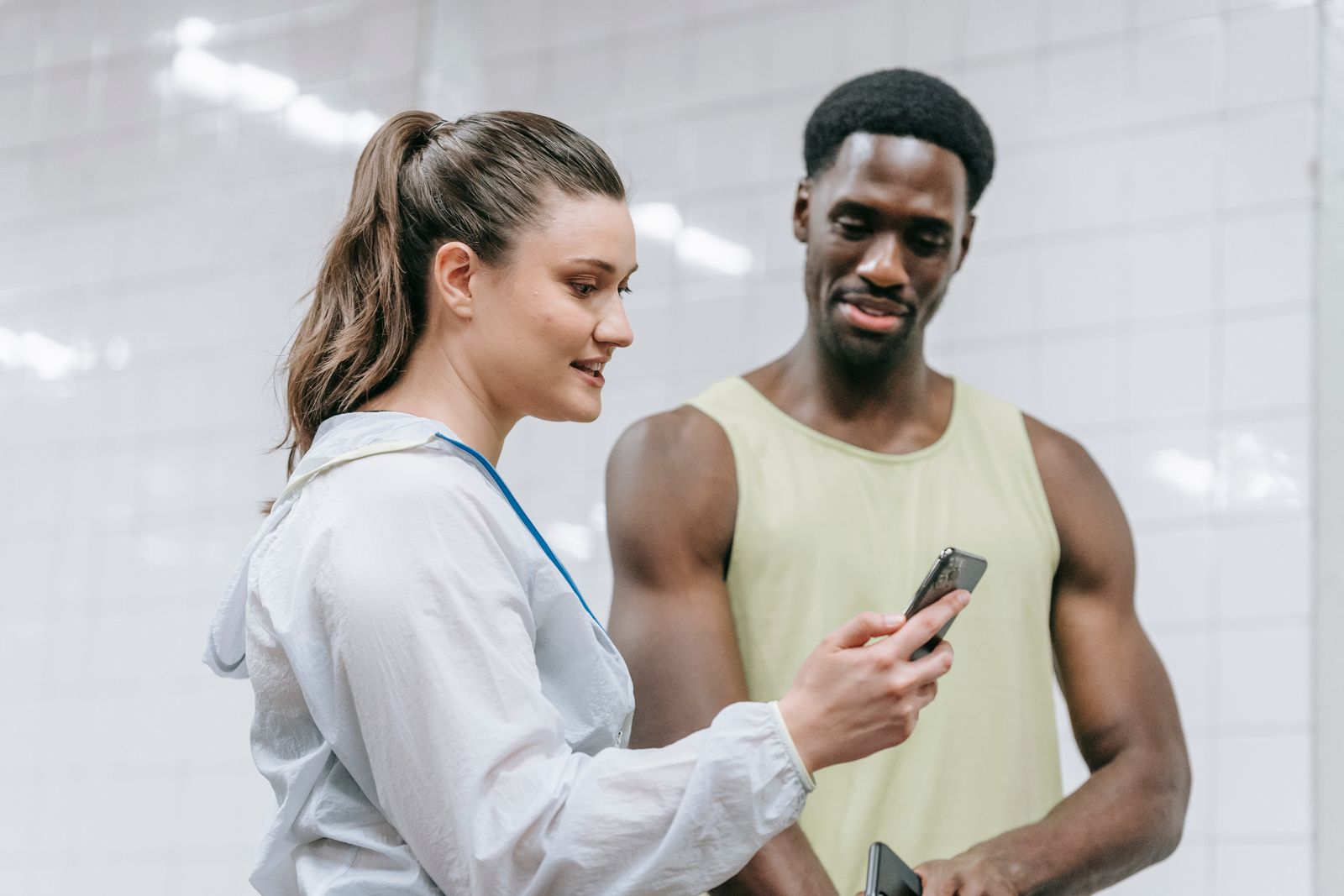 Personal Trainerin zeigt ihrem Kunden im Studio etwas auf dem Smartphone